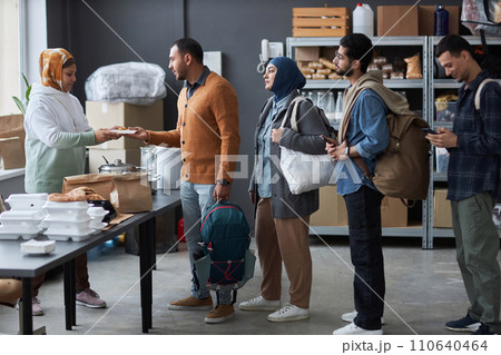 Full length side view of group of Middle Eastern people standing in line at refugee help center for free hot meals and supplies Full length side view of group of Middle Eastern people standing in line at refugee help center for free hot meals and supplies 110640464