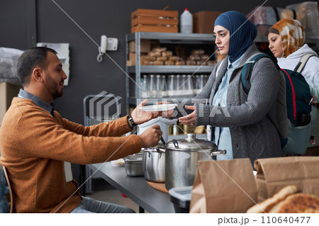 Side view portrait of Middle Eastern woman wearing hijab receiving hot meal at soup kitchen or refugee help center 110640477