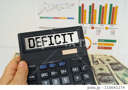 On the table there are financial reports, dollars, in the hands of a calculator with the inscription - Deficit 110641274