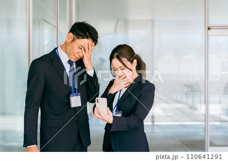 スマホを見てショックを受けるビジネスマンとビジネスウーマン（トラブル・悲報・失敗・不採用・不合格） 110641291