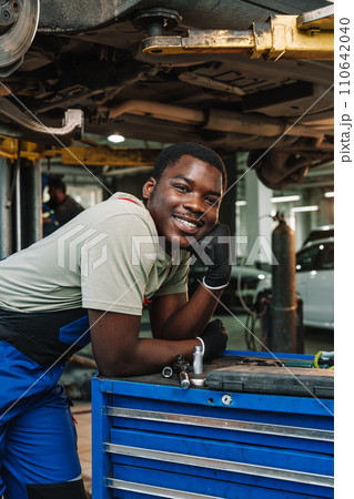 Portrait of young african man car service worker wearing uniform standing in garage Portrait of young african man car service worker wearing uniform standing in garage 110642040