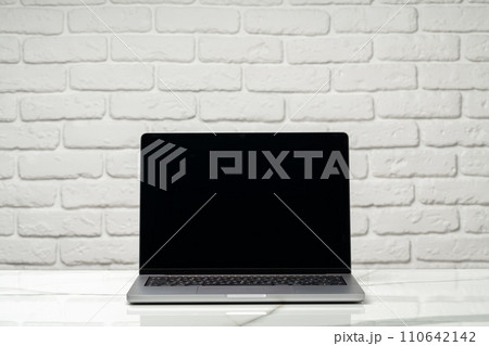 Laptop with black screen on desk against white brick wall 110642142