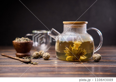 Teapot and glass cup with blooming tea flower inside on a wooden table 110643089