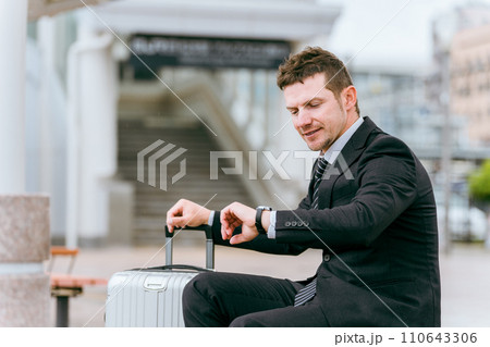 出張・旅行でバス停・タクシー乗り場・待合所で時間を確認する外国人ビジネスマン 出張・旅行でバス停・タクシー乗り場・待合所で時間を確認する外国人ビジネスマン 110643306