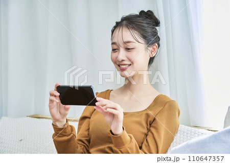 ルームウェアを着てスマートフォンの画面を見る若い女性 110647357
