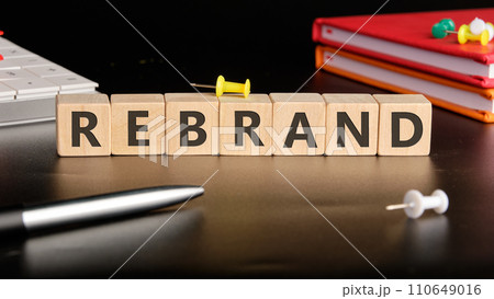 REBRAND the text of non-wooden cubes next to notepads, a calculator, a pen on a black background 110649016