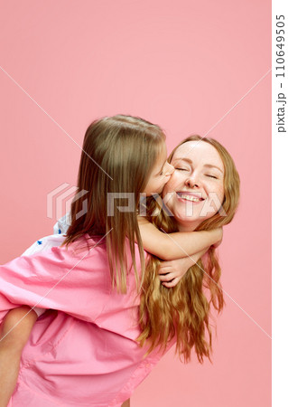 Happy smiling young woman, mother with her little daughter kissing her cheek against pink studio background. Mother's Day, International Happiness Day 110649505