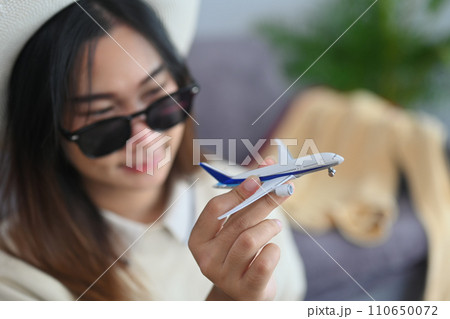 Happy young woman traveler in sunglasses holding airplane model. Traveling, vacation and transportation concept. 110650072
