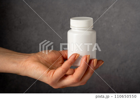 Female hand holding a white plastic bottle with pills. Capsules, collagen, vitamins, pain killers or drugs 110650550