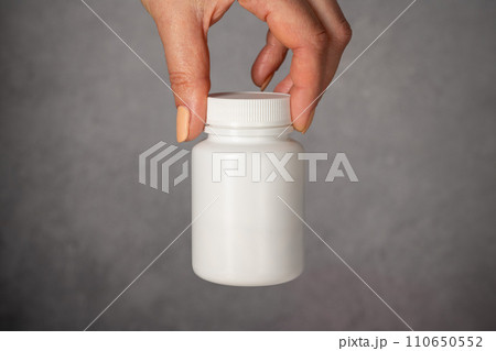 Female hand holding a white plastic bottle with pills. Capsules, collagen, vitamins, pain killers or drugs 110650552