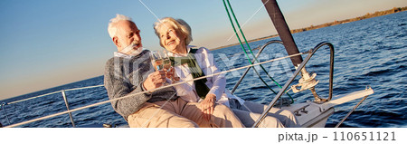 Happy senior couple in love drinking wine or champagne and laughing while celebrating wedding anniversary on a sailboat or yacht deck floating in a calm blue sea Happy senior couple in love drinking wine or champagne and laughing while celebrating wedding anniversary on a sailboat or yacht deck floating in a calm blue sea 110651121