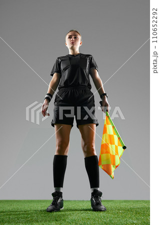 Young woman, female referee in uniform standing with flag, controlling game rules against grey studio background 110652292