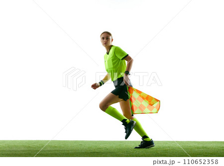 Assistant referee, young woman in uniform in motion on field, running with flag, leading control over game against white studio background Assistant referee, young woman in uniform in motion on field, running with flag, leading control over game against white studio background 110652358