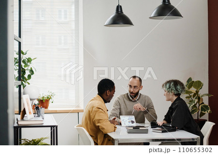 Young business people discussing graphs and charts on tablet screen while sitting at office 110655302