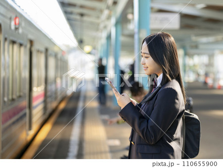 スマホを見ながら電車を待つ女子高校生 110655900