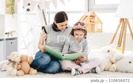 Lovely woman showing photo album to little girl in beautiful children's room 110656872