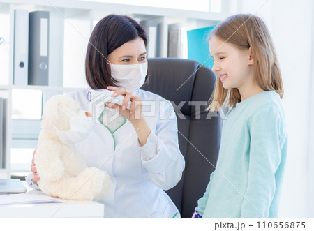Smiling little girl and kind doctor measuring tempertaure of teddy bear Smiling little girl and kind doctor measuring tempertaure of teddy bear 110656875