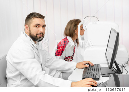 Teenage girl udergoes eye survey with doctor ophthalmologist on tomograph in clinic 110657013