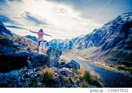Girl stand at the edge of the rock with raised hands and taking pleasure of breathtaking Andes landscape 110657022