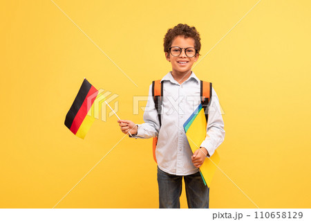 Grinning boy with German flag and school folders, yellow background 110658129