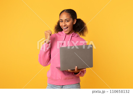 Excited black teenager girl with laptop making YES gesture, studio 110658132