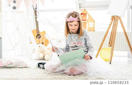 Beautiful little girl reading intersting book sitting on floor in children room 110658233