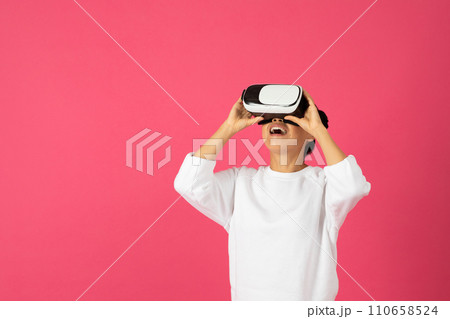 Excited Asian woman wearing VR headset, looking upwards with joyful expression Excited Asian woman wearing VR headset, looking upwards with joyful expression 110658524