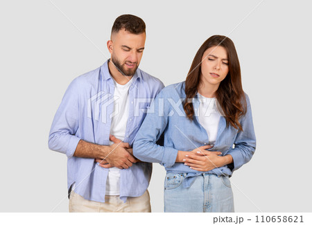 Couple with stomach ache, grimacing in discomfort on neutral background Couple with stomach ache, grimacing in discomfort on neutral background 110658621