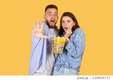 Couple with popcorn looking shocked, yellow background 110658717