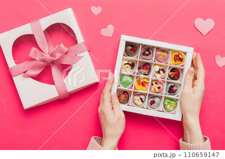 Female hands with delicious candies in box on color background 110659147