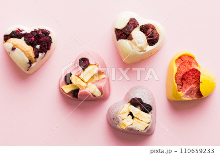 chocolate sweets in the form of a heart with fruits and nuts on a colored background. top view with space for text, holiday concept chocolate sweets in the form of a heart with fruits and nuts on a colored background. top view with space for text, holiday concept 110659233