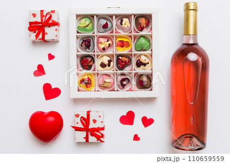 Bottle of red wine on colored background for Valentine Day with gift and chocolate. Heart shaped with gift box of chocolates top view with copy space Bottle of red wine on colored background for Valentine Day with gift and chocolate. Heart shaped with gift box of chocolates top view with copy space 110659559