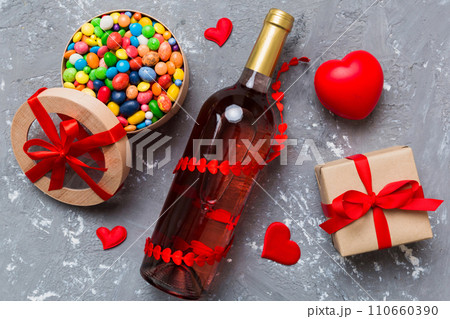 Bottle of red wine on colored background for Valentine Day with gift and chocolate. Heart shaped with gift box of chocolates top view with copy space Bottle of red wine on colored background for Valentine Day with gift and chocolate. Heart shaped with gift box of chocolates top view with copy space 110660390