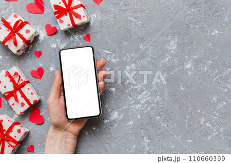 Woman hand holding mobile phone with blank screen on colored background with hearts, valentine day concept top view flat lay Woman hand holding mobile phone with blank screen on colored background with hearts, valentine day concept top view flat lay 110660399