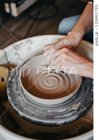 Decorating wet clay on a potter's wheel with a wine groove. A potter draws a spiral with his finger on the bottom of a white clay plate. Abstract clay background 110661785
