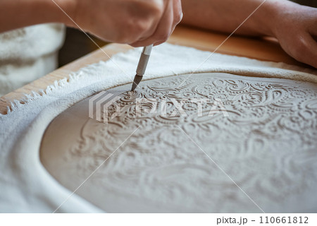 Potter is cutting out the shape of the future plate from the clay layer. Unplugging, hobby 110661812