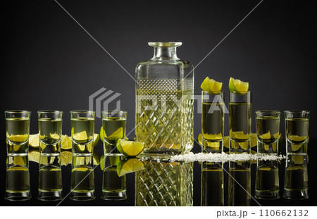 Tequila shots with lime slices and salt on a black reflective background. Tequila shots with lime slices and salt on a black reflective background. 110662132
