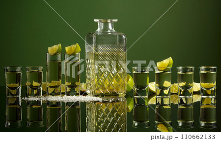 Tequila shots with lime slices and salt on a green background. 110662133