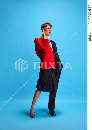 Duet of masculine and feminine voices. Full-length portrait of young attractive male model with female and male make-up talking on phone. 110662692