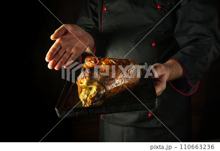 Baked duck carcass on a baking sheet in the hands of a chef. Concept of cooking delicious poultry. Dark space for advertising 110663236