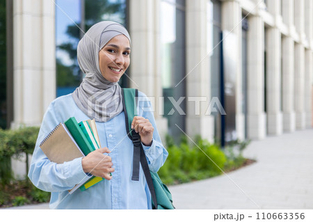 An elegant young Muslim woman in hijab carrying books, happily walking in a business district, reflecting urban professional life. An elegant young Muslim woman in hijab carrying books, happily walking in a business district, reflecting urban professional life. 110663356