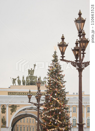The main Christmas tree shimmers with lights of decorations through vintage lamppost, the central Palace square of the city decorated for the celebration during the snowfall, Arch of the General Staff The main Christmas tree shimmers with lights of decorations through vintage lamppost, the central Palace square of the city decorated for the celebration during the snowfall, Arch of the General Staff 110663528