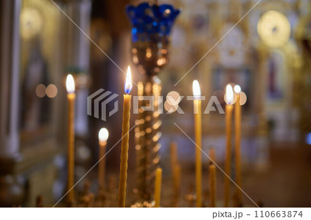 Burning church candles in a gilded candlestick in a temple in the dark Burning church candles in a gilded candlestick in a temple in the dark 110663874