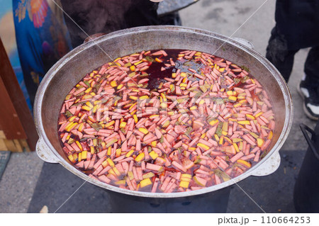 Round grill in the shape of a bowl with fire inside. A man prepares a hearth for barbecue. The round hearth is cleaned before cooking. The firewood lies in the bowl of the outdoor hearth. 110664253