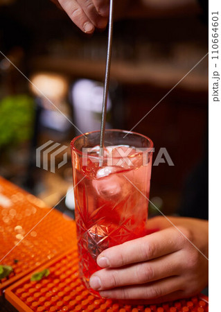 barman gently pours finished cocktail from glass shaker into glass. Body of bartender 110664601