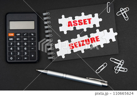 On the table is a calculator, a pen and a notebook with the inscription - Asset Seizure 110665624