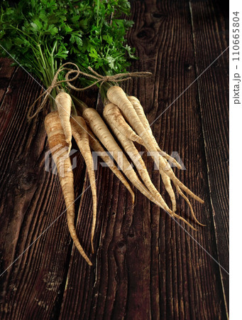 Bunch of parsley roots with green leaves on dark wooden board Bunch of parsley roots with green leaves on dark wooden board 110665804
