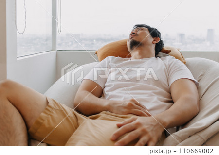Asian man rest and relaxed on bean bag sofa in the apartment on weekends Asian man rest and relaxed on bean bag sofa in the apartment on weekends 110669002
