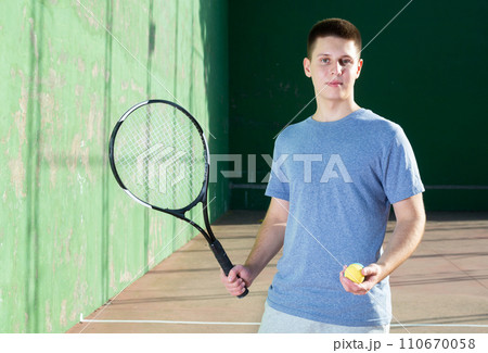 Smiling young frontenis player standing on open-air fronton court Smiling young frontenis player standing on open-air fronton court 110670058