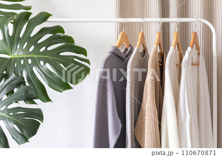 White hanger with beautiful clothes in neutral colors. Monstera flower with large leaves. 110670871